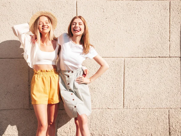 流行の夏服の2人の若い美しい笑顔のヒップスター女性 帽子の白い壁の近くの通りにポーズ性的屈託のない女性 正の純粋なモデル楽しいです日没時 — ストック写真