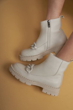 Bej çizmeli, deri ayakkabılı, stüdyo fotoğraflı şık bir kadın. Sarı pastel arka planda günlük konsept fotoğraf.