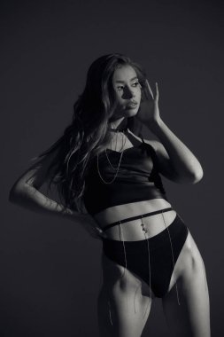 Stüdyo portresi, esmer, kıvırcık saçlı, siyah elbiseli, yüksek topuklu, bronz tenli uzun bacaklı, ince vücutlu, arka planda güneş ışığıyla kalan çekici bir kadın modeli..