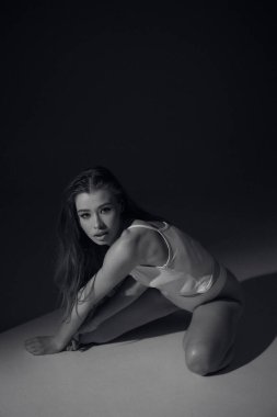 Kahverengi uzun kıvırcık saçlı, beyaz elbiseli, bronz tenli uzun bacaklı, ince vücutlu, arka planda güneş ışığı altında oturan çekici bir kadın modeli. Güzel, zarif bir vücut konsepti, pozitif, sağlıklı bir yaşam tarzı.