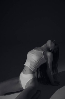 Kahverengi uzun kıvırcık saçlı, beyaz elbiseli, bronz tenli uzun bacaklı, ince vücutlu, arka planda güneş ışığı altında oturan çekici bir kadın modeli. Güzel, zarif bir vücut konsepti, pozitif, sağlıklı bir yaşam tarzı.