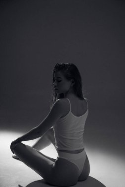 Kahverengi uzun kıvırcık saçlı, beyaz elbiseli, bronz tenli uzun bacaklı, ince vücutlu, arka planda güneş ışığı altında oturan çekici bir kadın modeli. Güzel, zarif bir vücut konsepti, pozitif, sağlıklı bir yaşam tarzı.