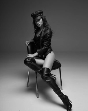 Siyah deri ceketli ve çizmeli kız. Güzel, genç ve zarif bir kadının yüksek moda portresi. Siyah beyaz stüdyo resmi, yumuşak gri arka plan. Tam boy portre