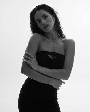 Siyah elbiseli, ince vücutlu, uzun kıvırcık saçlı, çekici bir kadın modelin portresi. Güzel, zarif bir kişilik, vücut pozitifliği, sağlıklı yaşam tarzı. Beyaz arkaplan.