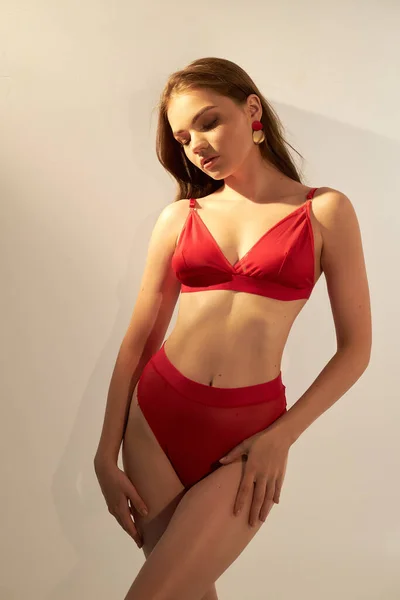 白い背景に赤いセクシーな水着で長い巻き毛の美しい女性 ファッションに身を包んだ完璧な肌を持つ若い女性モデル 日光浴 日焼け止めコンセプト — ストック写真