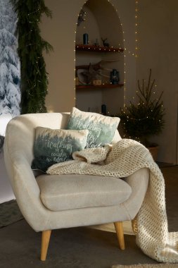 cozy corner in the New Year's room, a comfortable white soft chair with pillows and plaid bedspread