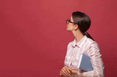 Kitabı olan zeki genç bir kadın kırmızı afiş arkaplanına bakıyor.