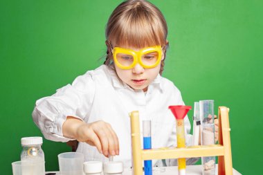 Yeşil arka plan üzerinde bilimsel deneyleri olan küçük bir kız.
