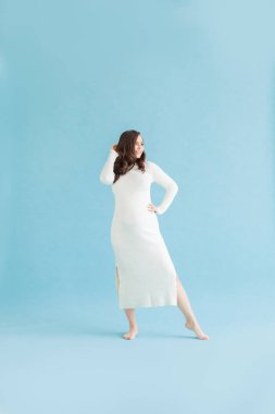 Pretty pregnant woman in white cotton dress standing on blue background