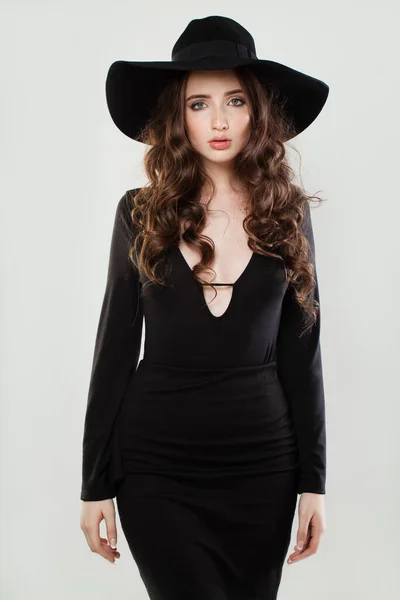 黒のドレスと帽子を身に着けている長い 健康的で光沢のある巻き毛を持つブルネットの女性白い背景 — ストック写真