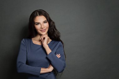 Mutlu güzel kadın gülümsüyor ve kollarını kavuşturup gri arka planda duruyor..