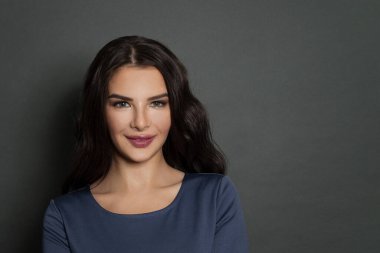 Koyu gri arka planda güzel, dalgalı saçlı güzel bir kadının yakın plan portresi.