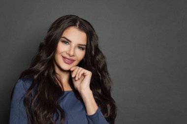 Kıvırcık saçlı güzel esmer kadın gülümsüyor.