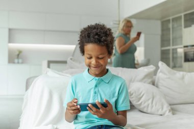 Akıllı telefonlu mutlu çocuk. Annesinin evde telefonu var ve geçmişi bulanık.