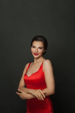 İpeksi kırmızı bir elbise giymiş, siyah üzerine poz veren güzel bir esmer kadın.