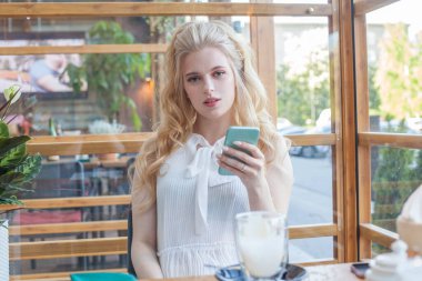 Kafede kahve içip akıllı telefon kullanan mükemmel bir kadın.
