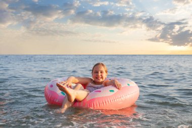 Mutlu çocuk denizde pembe şişirilebilir yüzükle rahatlıyor.