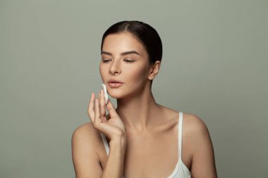 Gözleri ve yüzü kapalı hoş bir kadın pamuklu mendille cildini temizler.