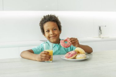 Portakal suyu ve beyaz çöreklerle tatlı, zeki bir çocuk.