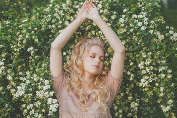 Young pretty woman resting on white spring flowers and green leaves outdoors