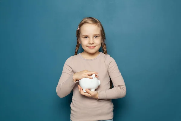 Child Girl Holding White Piggy Bank Her Hands Blue Background — Stock Photo, Image