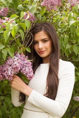 Elinde bahar leylağı buketi tutarken kameraya gülümseyen neşeli kadın.