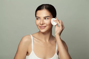 Güzel genç bir kadın makyajını siliyor ve gri arka plana bakıyor.