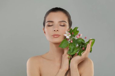Çiçekli güzel bir kadın yüzü. Gri arka planda dinlenen bahar kadını, stüdyo portresi