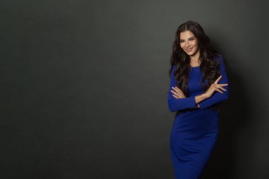 Uzun ve parlak dalgalı saçlı, gülümseyen ve kolları çapraz duran esmer kadın. Mavi elbiseli güzel manken.