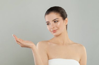 Şirin, mutlu, gülümseyen, gri arka planda elini açık tutan güzel bir genç kadın.