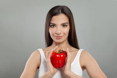 Kırmızı dolma biber tutan ve gülümseyen, sıradan kıyafetler giyen neşeli, tatlı bir kadın.