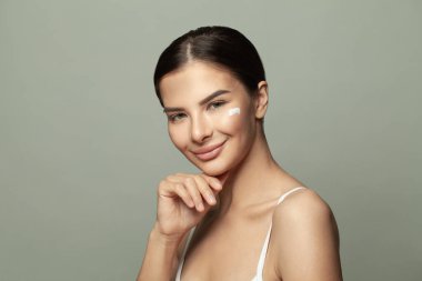 Neşeli güzel kadın yüzüne krem sürüyor, güzellik tedavileri cildine önem veriyor.