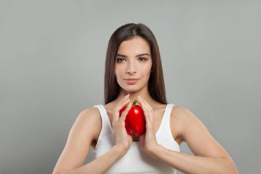 Gri stüdyo arka planında kırmızı biber tutan hoş bir kadın.