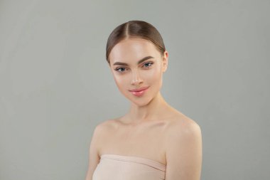 Gri stüdyo arka planında gülümseyen güzel bir kadın, portre. Yüz bakımı, cilt bakımı ve doğal güzellik kavramı
