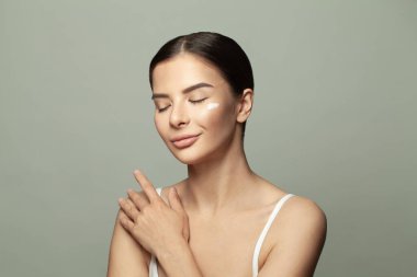 Oldukça çekici bir kadın dokunuyor, mükemmel teninin keyfini çıkarıyor gri stüdyo arka planında izole edilmiş.