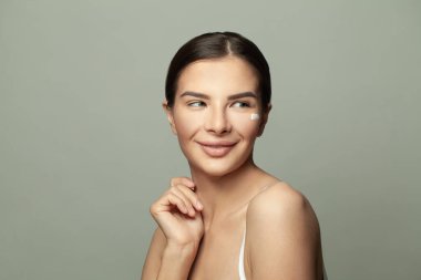 güzel genç kadın uygulanan yüz kremi gülümseyen ve uzağa arıyorsunuz