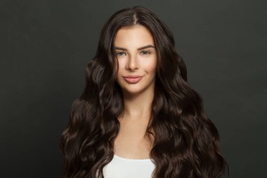 Siyah arka planda gülümseyen uzun kıvırcık saçlı tatlı bir kadın.