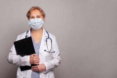 Tıbbi maskeli kıdemli doktor ve steteskoplu beyaz önlüklü kadın. 