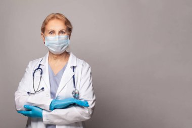 Beyaz üniformalı profesyonel kendine güvenen olgun bir doktor, boynunda steteskop, arka planda hastaya yardım etmeye hazır.