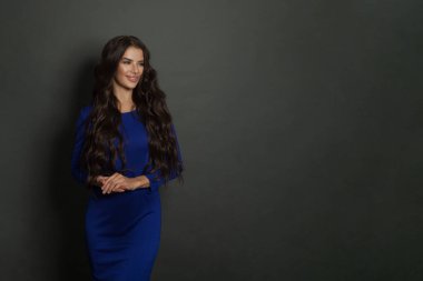 Uzun, sağlıklı saçları ve güzel elbisesi olan, koyu gri arka planda fotokopi alanı olan güzel bir bayan. Çekici esmer kadın gülümsüyor