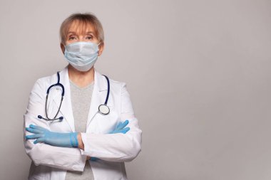 Beyaz üniforma giyen yaşlı kadın doktor portresi gri stüdyo arka planında izole edilmiş, yetişkin kadın hemşire ya da kameraya bakan steteskoplu pratisyen kadın. Sağlık hizmetleri kavramı