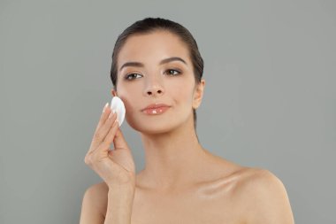 Pamuklu ped tutan güzel esmer kadın makyaj malzemesi çıkartıyor. Yüz derisi gri arka planda mikiler su etkisi yapıyor.