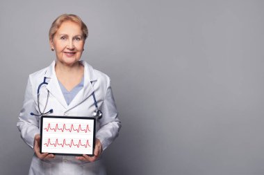 Gülümseyen doktor kalp atışı ve kardiyogramla dijital tablet gösteriyor.