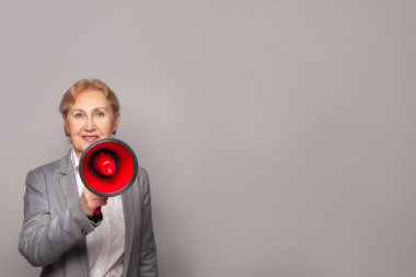 Mutlu kıdemli iş kadını hoparlöre bağırıyor Gri duvar afişi arka planında kopya alanı ile
