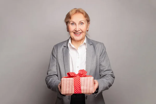 Happy surprised woman senior lady posing with gift box on grey background