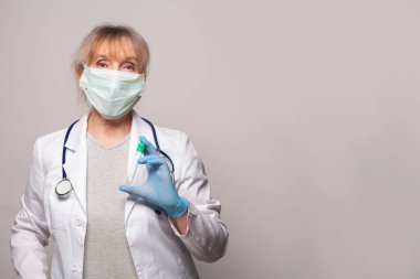 Gri duvarda yeşil test tüpü olan olgun bir kadın doktor.