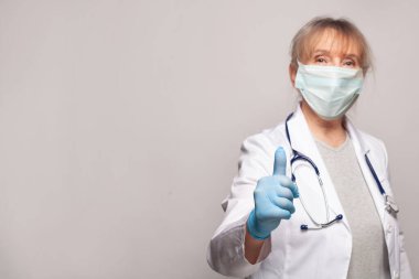 Tıbbi maskeli doktor gri pankartta baş parmağını gösteriyor.