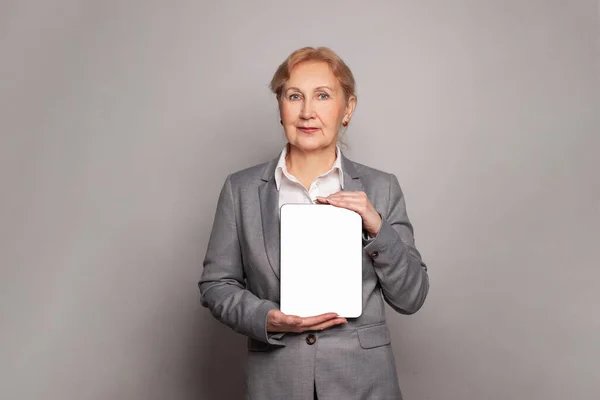 灰色の背景に立って空のデジタルタブレットとスマート自信のあるシニアビジネス女性 — ストック写真