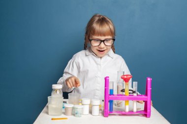 Okulun laboratuarında mavi arka planda bilim deneyleri yapan mutlu kız öğrenci.