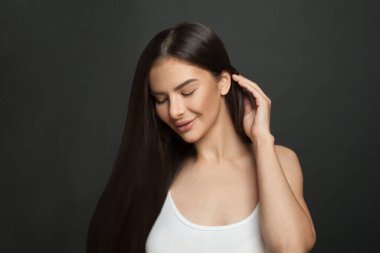 Siyah arka planda gülümseyen uzun düz saçlı güzel esmer kadın portresi.